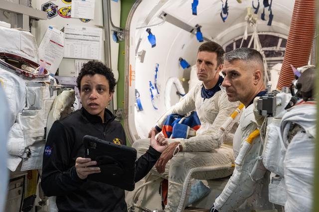 Astronaut Jessica Watkins assists astronauts Josh Kutryk and Luke Delaney as they practice suiting up in spacesuits